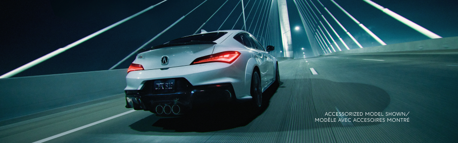 ¾ rear view of white Integra Type S driving away from camera over an empty bridge at night.