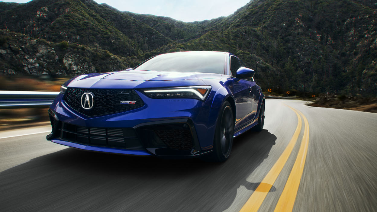 3/4 front view of blue Integra Type S driving on mountainous highway.