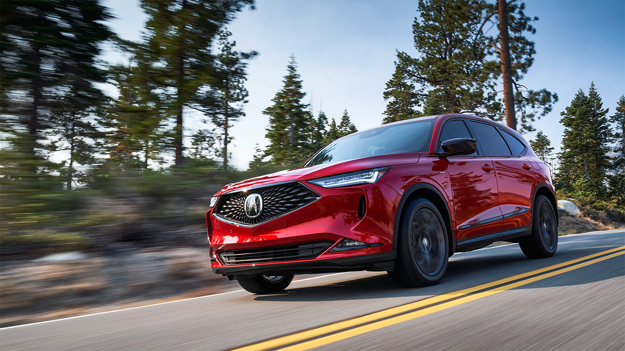 Un MDX rouge emprunte une route en pleine nature.