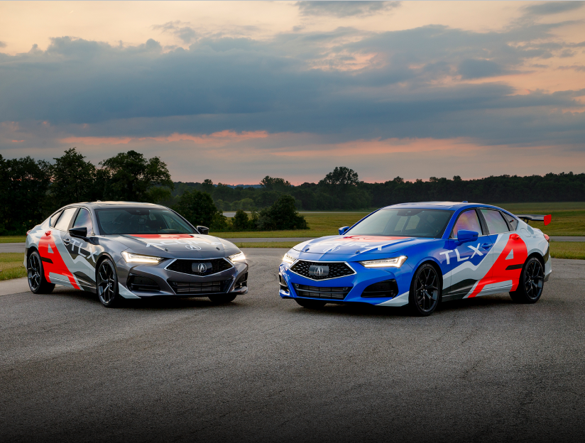 A grey and a blue Acura TLX, both with red and grey sponsorship wraps, parked slightly facing each other in front of an open field with trees in the background. Deux Acura TLX, l’une grise et l’autre bleue, recouverte d’un habillage personnalisé rouge et gris, stationné en angle l’une en face de l’autre devant un terrain gazonné et des arbres.