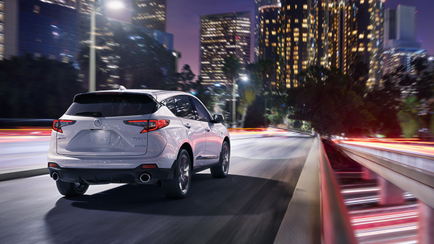 An Acura RDX drives through a city at night.  /  Un Acura RDX roulant dans une ville la nuit. 