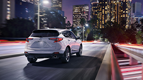 An Acura RDX drives through a city at night.  /  Un Acura RDX roulant dans une ville la nuit. 